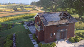 Haus mit Photovoltaikanlage vor Feldern mit Windrädern