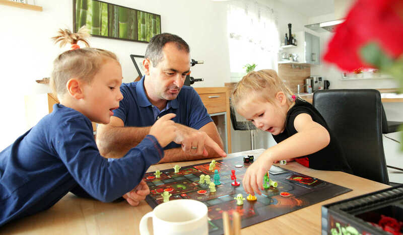 Vater spielt gemeinsam mit den Kindern ein Brettspiel im Esszimmer